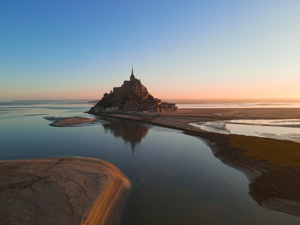 um castelo sentado no topo de uma praia ao lado de um corpo de água