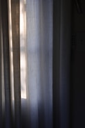 Vertical draped curtains partially illuminated by soft, natural light filtering through a window, creating a peaceful and serene ambiance.