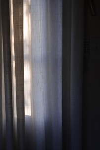 Vertical draped curtains partially illuminated by soft, natural light filtering through a window, creating a peaceful and serene ambiance.