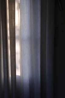 Vertical draped curtains partially illuminated by soft, natural light filtering through a window, creating a peaceful and serene ambiance.
