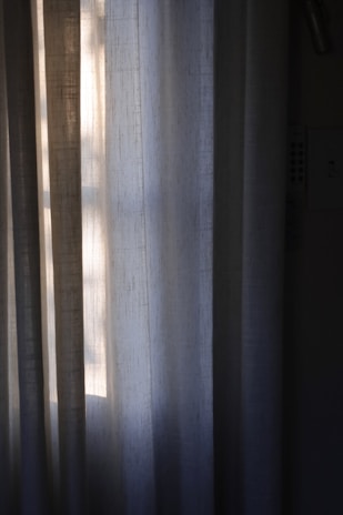 Vertical draped curtains partially illuminated by soft, natural light filtering through a window, creating a peaceful and serene ambiance.