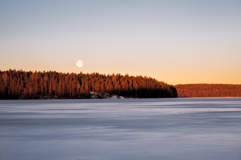 a full moon rising over a snowy lake