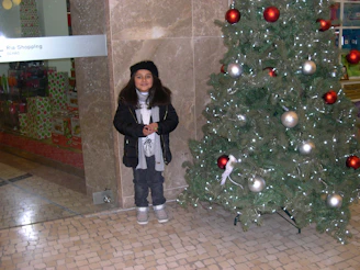 A little girl in a cozy winter jacket from the Christmas collection, standing by a decorated tree