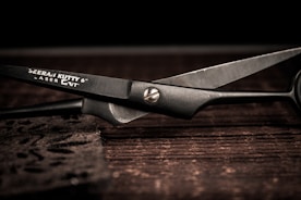 Pair of scissors with freshly sharpened blades resting on a dark wooden surface.