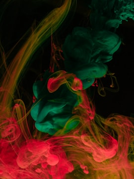 Vibrant swirls of green and red ink gently blend together in a dark liquid environment, creating intricate patterns and textures.