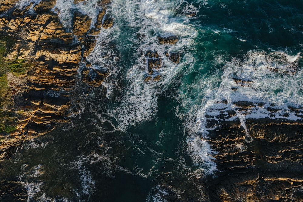 an aerial view of the ocean with waves crashing on the rocks