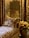 A luxurious interior setting with ornate wall coverings and curtains featuring intricate patterns. A plush, patterned cushion rests on an upholstered couch, also detailed with elaborate designs. A metallic pot holds vibrant orange flowers, adding a touch of color to the scene.