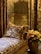 A luxurious interior setting with ornate wall coverings and curtains featuring intricate patterns. A plush, patterned cushion rests on an upholstered couch, also detailed with elaborate designs. A metallic pot holds vibrant orange flowers, adding a touch of color to the scene.