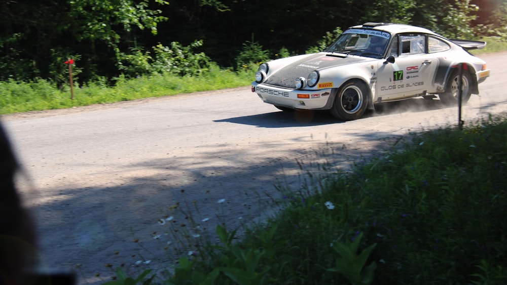 a white car driving down a road next to a forest