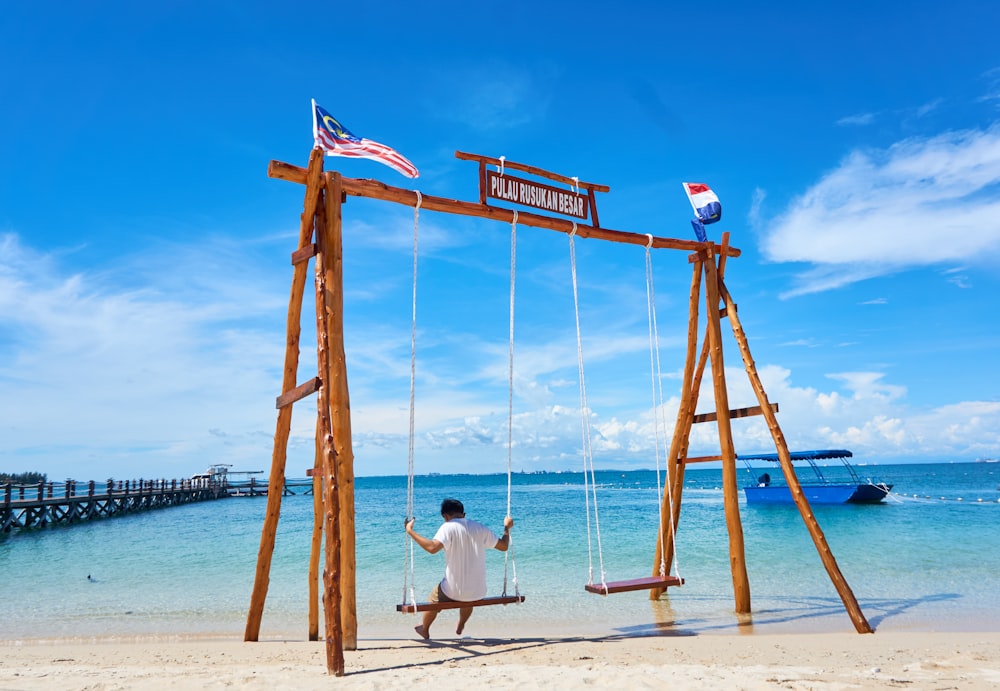 a man is sitting on a swing at the beach