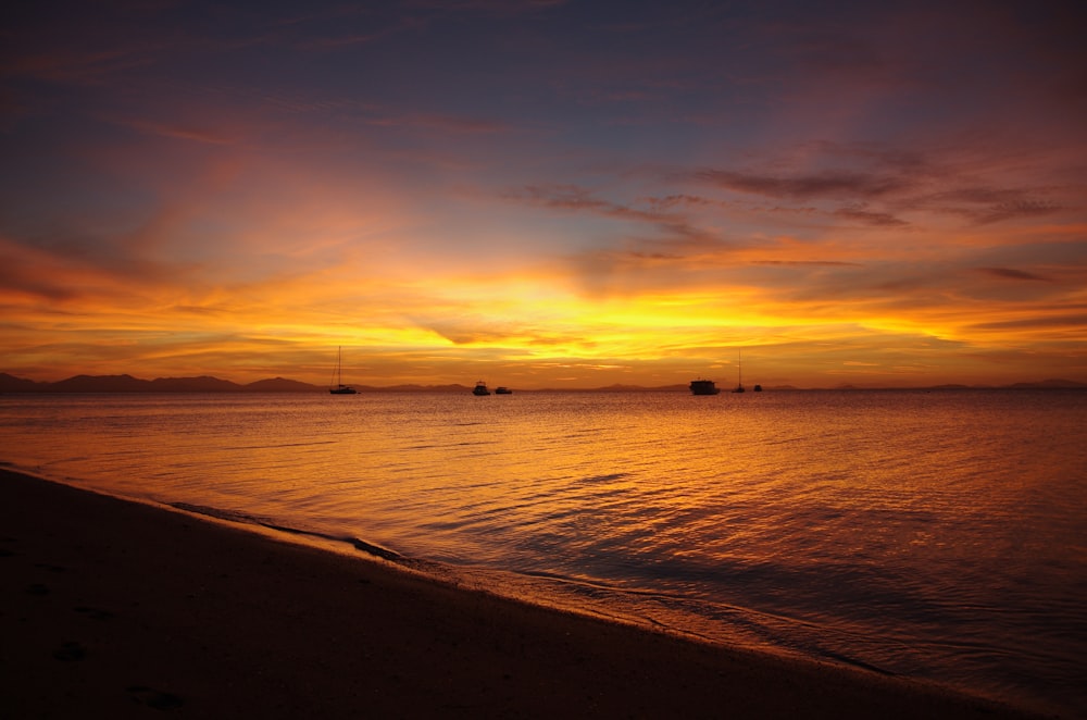 a sunset on a beach with boats in the water