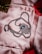 A silver necklace with a pendant shaped like an eye, encrusted with small stones, lies on a soft pink fabric. The chain is silver and twisted, forming a loop around the pendant. In the background, there are parts of two small boxes, one brown with a golden ribbon and the other red.