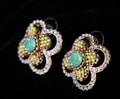 Two ornate earrings with a floral design featuring a central turquoise stone surrounded by small multicolored beads. Each petal-like section is bordered by a series of clear gemstones, creating a sparkling effect against a dark background.