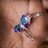 A pair of earrings with faceted, colorful gemstones held in a hand. The gemstones have a combination of blue, purple, and teal colors, and the earrings have metal clasps.
