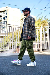 A man dressed in a casual yet sharp outfit featuring a denim jacket and white sneakers, walking through a park.
