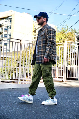 A man dressed in a casual yet sharp outfit featuring a denim jacket and white sneakers, walking through a park.