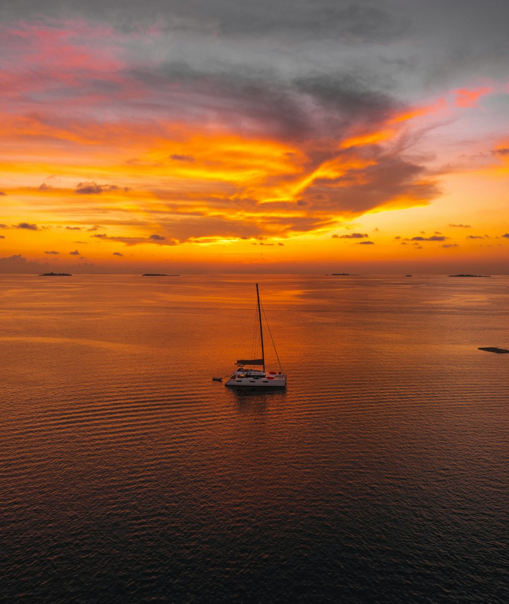 a sailboat floating in the middle of the ocean at sunset