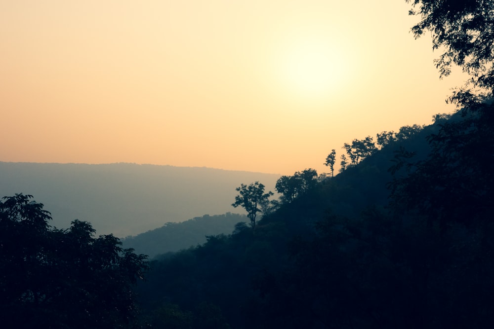 the sun is setting over the mountains and trees