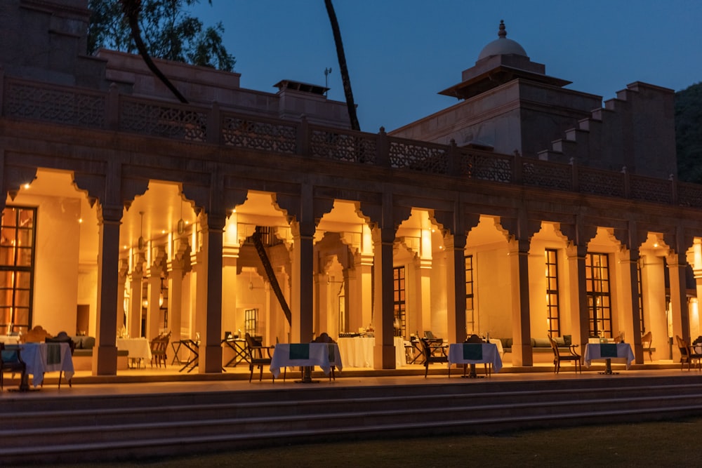 a building lit up at night with tables and chairs