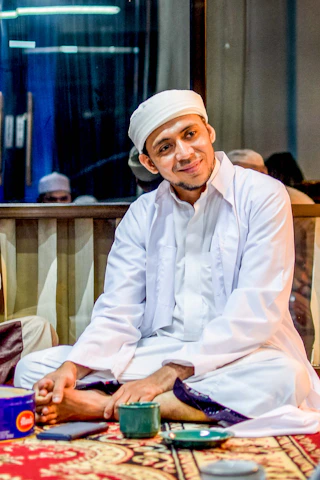 A Muslim man in modest business attire working thoughtfully at a sleek, modern workspace in Boston.