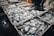 A collection of freshly caught fish stacked in white crates. The fish appear shiny and wet, likely indicating they have been recently taken from the water. The scene seems to be at a market or fishery with a concrete floor partially visible and some human activity in the background.
