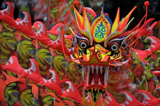 A vibrant and intricately designed dragon head with bold colors and detailed patterns. The dragon features sharp teeth, large eyes, and various swirling designs in its skin, with red, yellow, and orange hues dominating its appearance.