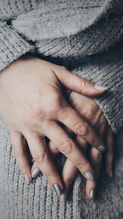 Soft, nude-toned nails with subtle shimmer resting against a cozy sweater fabric.