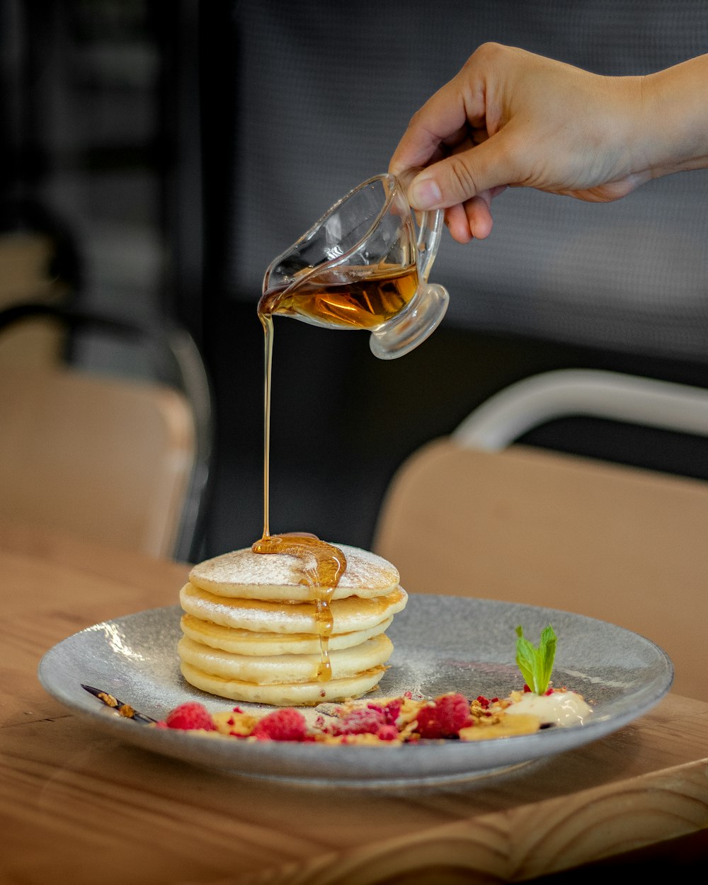 a person pouring syrup on a stack of pancakes