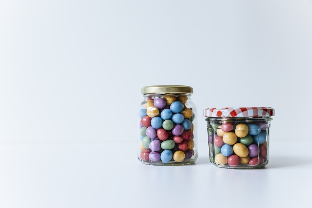 deux bocaux en verre remplis de bonbons sur une surface blanche