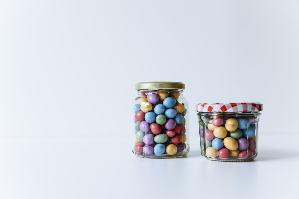 two glass jars filled with candy beans on a white surface