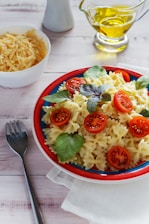 A colorful bowl of fresh pasta with cherry tomatoes and basil on a rustic wooden table.