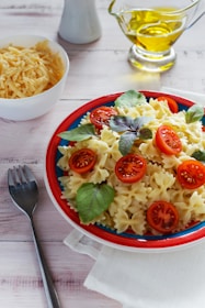 A colorful bowl of fresh pasta with cherry tomatoes and basil on a rustic wooden table.