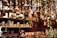 A variety of colorful, handcrafted ornaments and ceramics are displayed on shelves and hanging from above. The ornaments include small houses with conical roofs and various whimsical shapes with intricate patterns. The shelves are filled with mugs and other pottery pieces, some wrapped in protective material.
