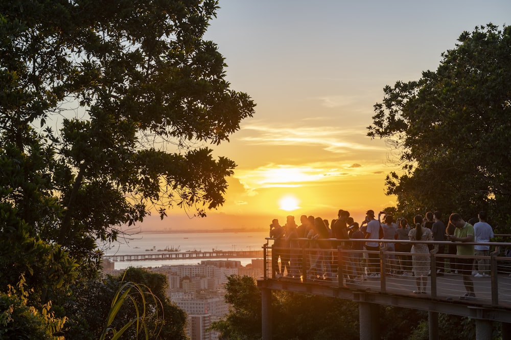 a group of people standing on a bridge at sunset