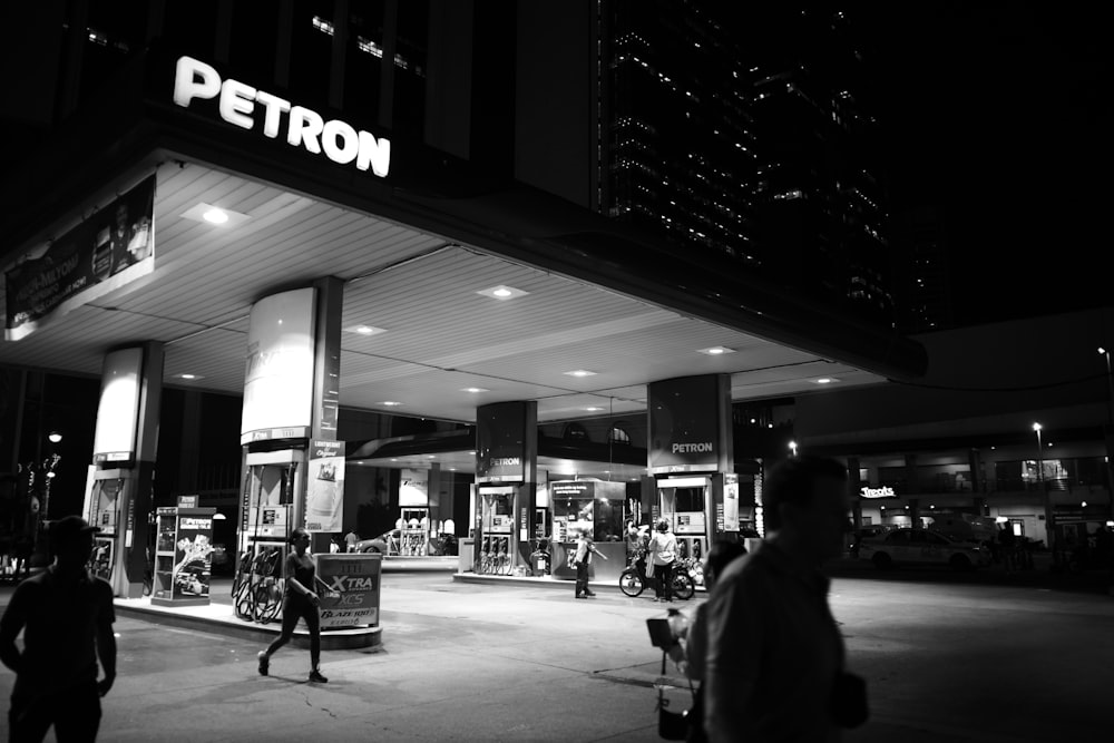 a black and white photo of people walking in front of a petrol station