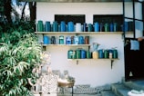 Set of colorful enamel storage canisters arranged neatly on a wooden shelf with fresh herbs nearby.