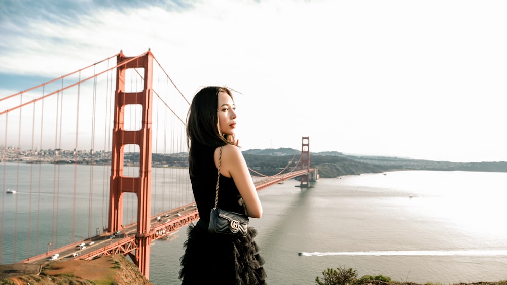 a woman in a black dress standing in front of the golden gate bridge