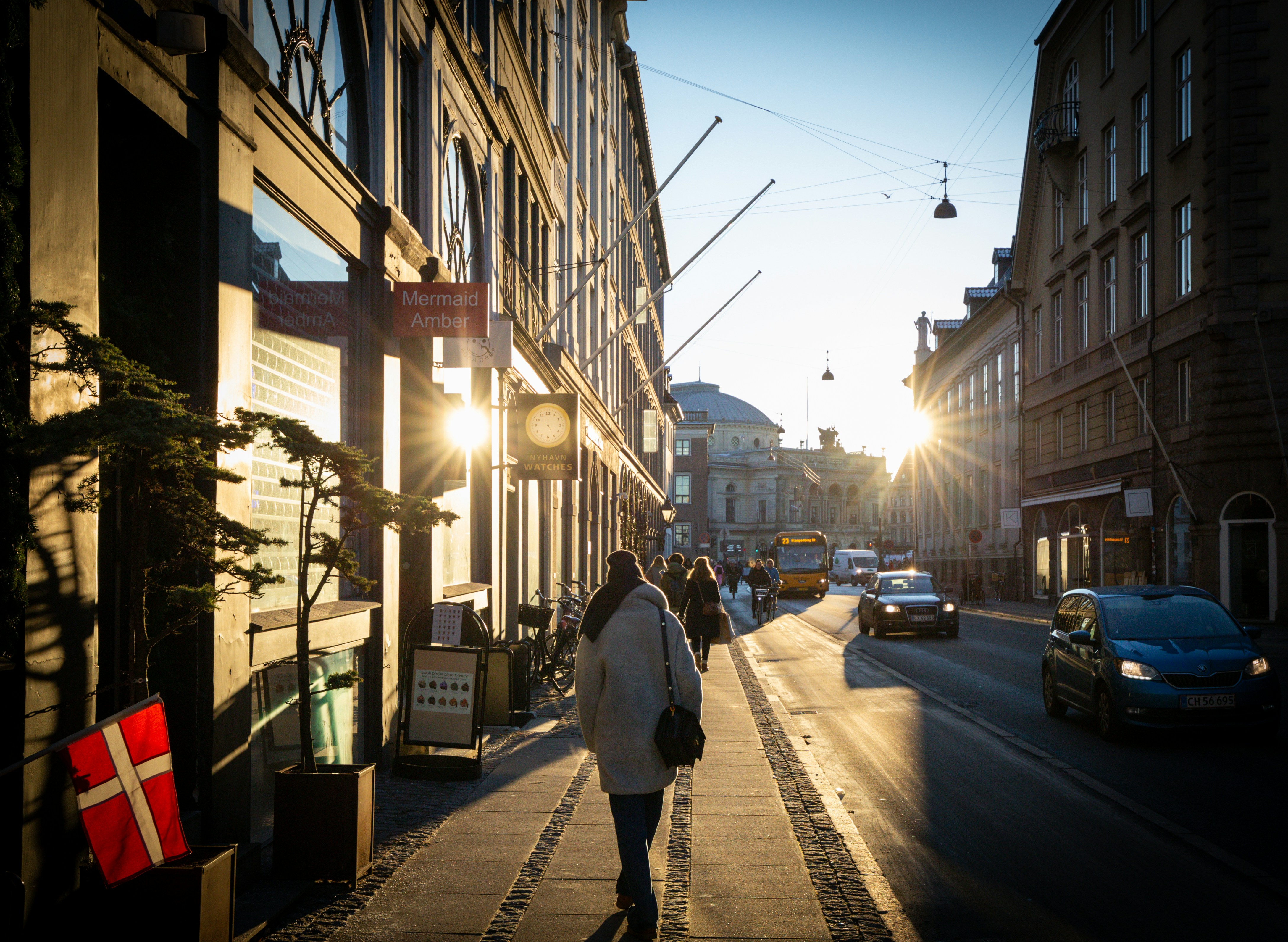 a woman walking down a street next to tall buildings in copenhagen