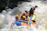 A group of people wearing helmets and life jackets are paddling a colorful inflatable raft through turbulent white-water rapids. Water splashes around them as they navigate the river with focused expressions.