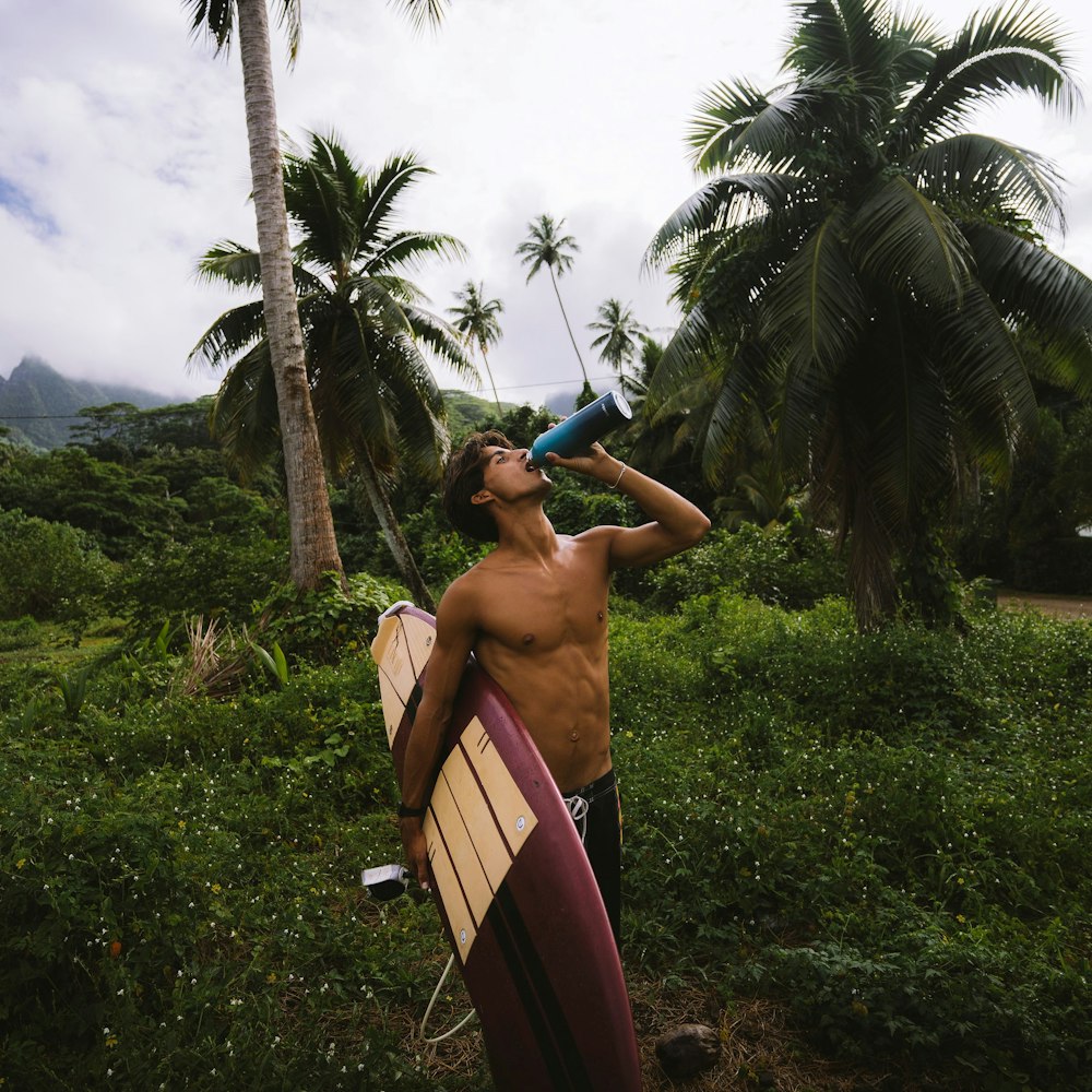a man drinking from a bottle while holding a surfboard