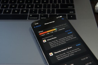 A smartphone displaying the iPhone storage management screen is placed on a laptop keyboard. The screen shows details about the storage used by different applications, with a focus on iCloud Photos. The image conveys a sense of digital organization and technology usage.