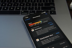 A smartphone displaying the iPhone storage management screen is placed on a laptop keyboard. The screen shows details about the storage used by different applications, with a focus on iCloud Photos. The image conveys a sense of digital organization and technology usage.