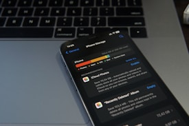 A smartphone displaying the iPhone storage management screen is placed on a laptop keyboard. The screen shows details about the storage used by different applications, with a focus on iCloud Photos. The image conveys a sense of digital organization and technology usage.