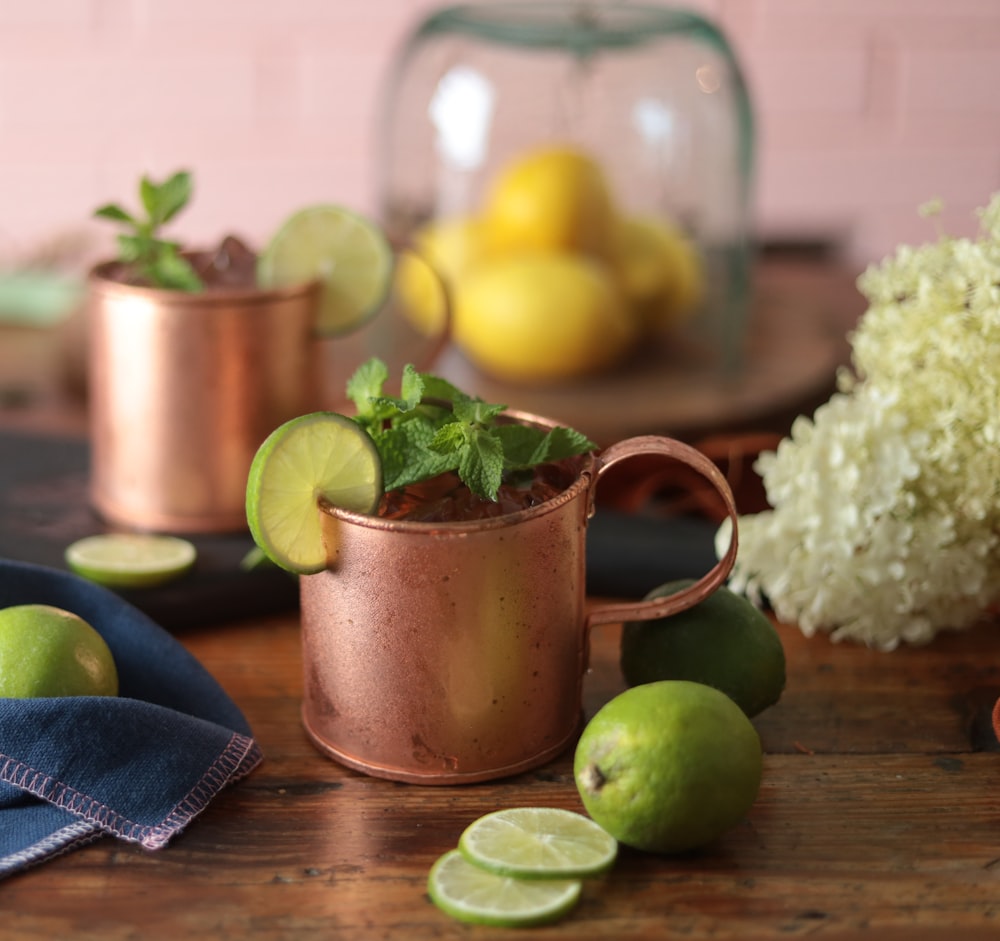 a copper mug with limes and limes on a table