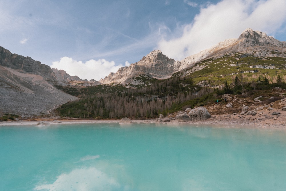 a blue lake surrounded by mountains under a cloudy sky