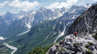 A hiker standing on a mountain peak overlooking a vast green valley.