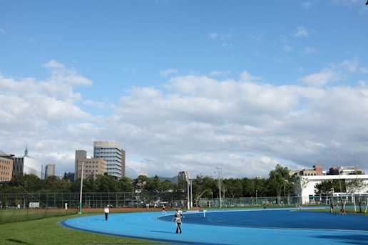 Construction workers laying down a running track surface under a clear blue sky.