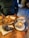 A wooden table holds a variety of pastries and two cups of coffee. Two croissants on a blue-rimmed plate and a unique black croissant on a separate plate are arranged neatly. The coffee cups feature latte art on their creamy surfaces, placed on saucers with a silver tray underneath.