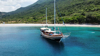 A luxury sailboat anchored near a quiet beach with crystal clear water.