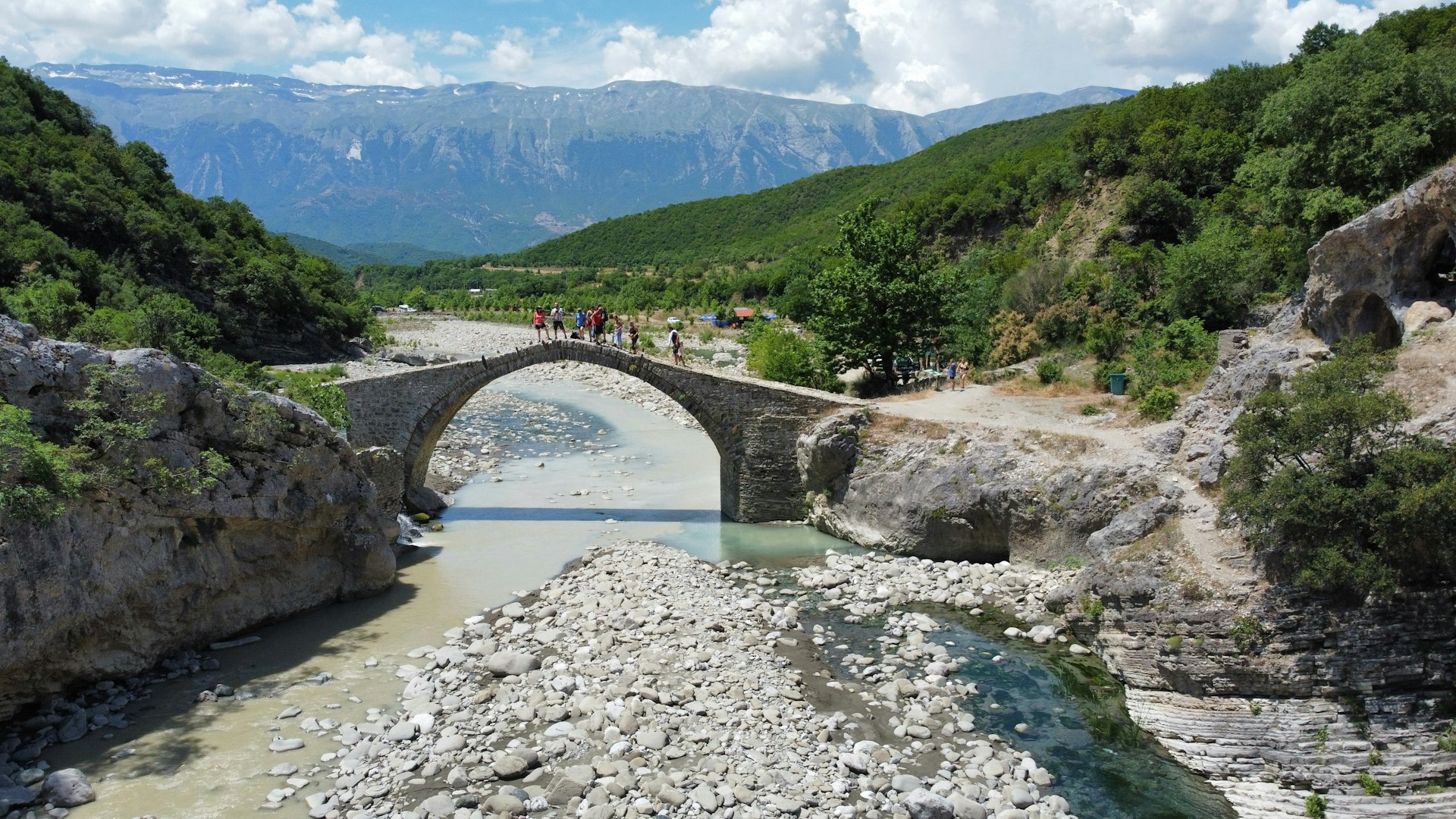 a stone bridge over a river surrounded by mountains